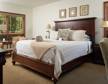 California King bed with White bedspread, Wood frame bed with High Headboard. Large windows with a view of the mountains